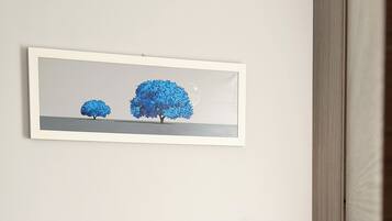 Un salon moderne avec un canapé en cuir gris, une table basse en bois et une œuvre d’art encadrée représentant des arbres bleus, accrochée au mur.