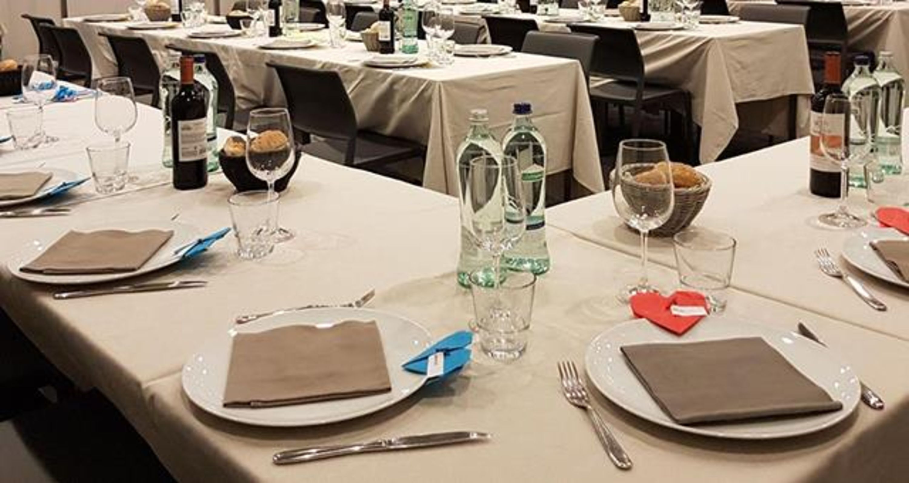 Un salón de banquetes con mesas dispuestas para un evento formal, cada una con platos, cubiertos y botellas de agua.