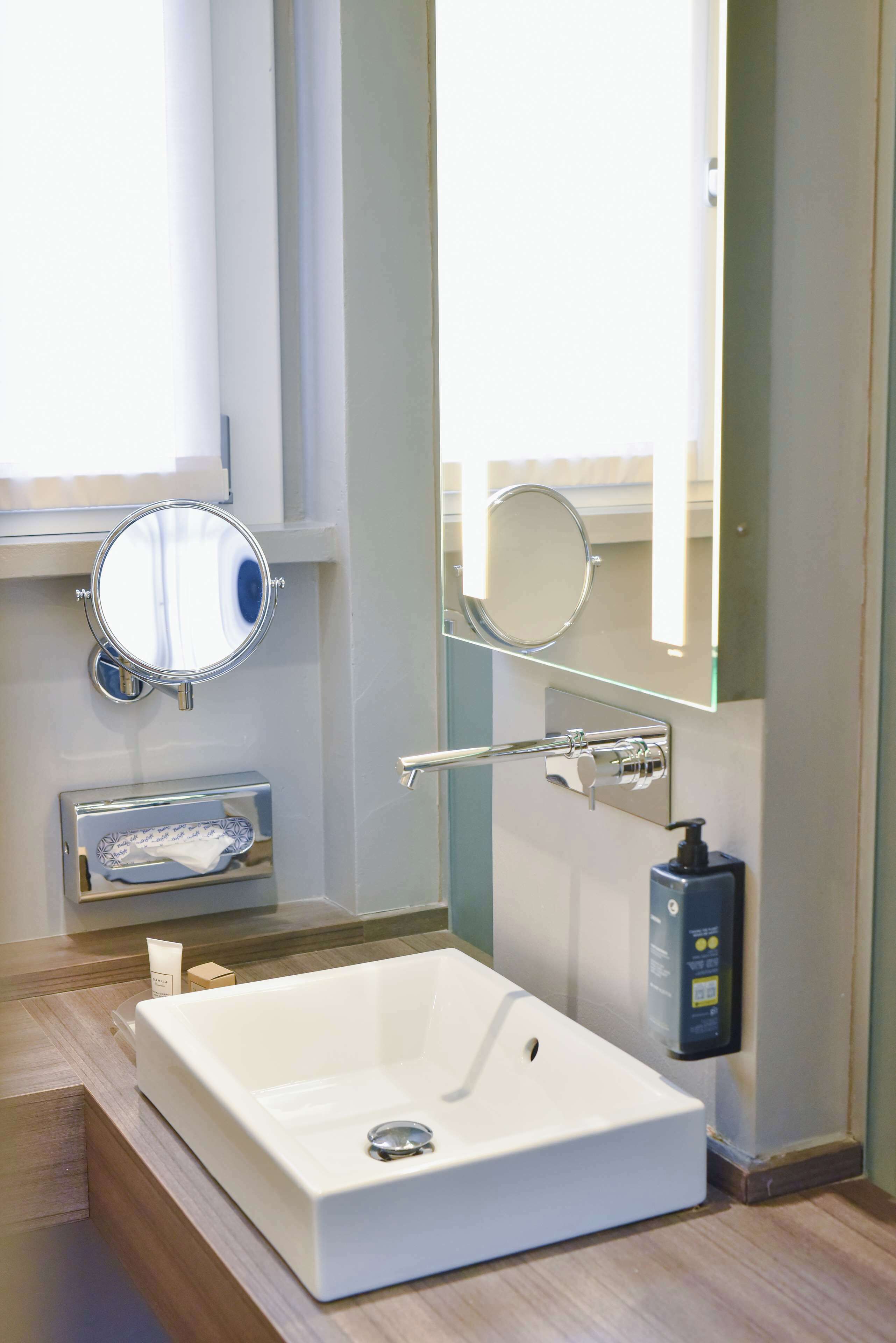 Een moderne badkamer met een groot, wit bad, een ronde spiegel en een zeepdispenser.