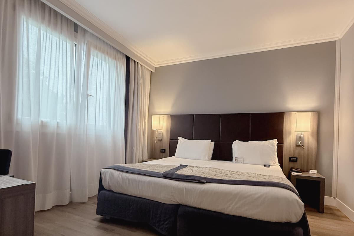 A hotel room with a large bed, two bedside tables, a desk, and a chair.