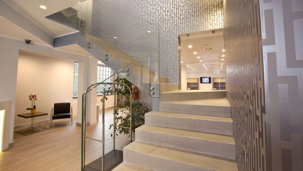 Un interior moderno con una escalera, barandillas de cristal y una pared con diseño.