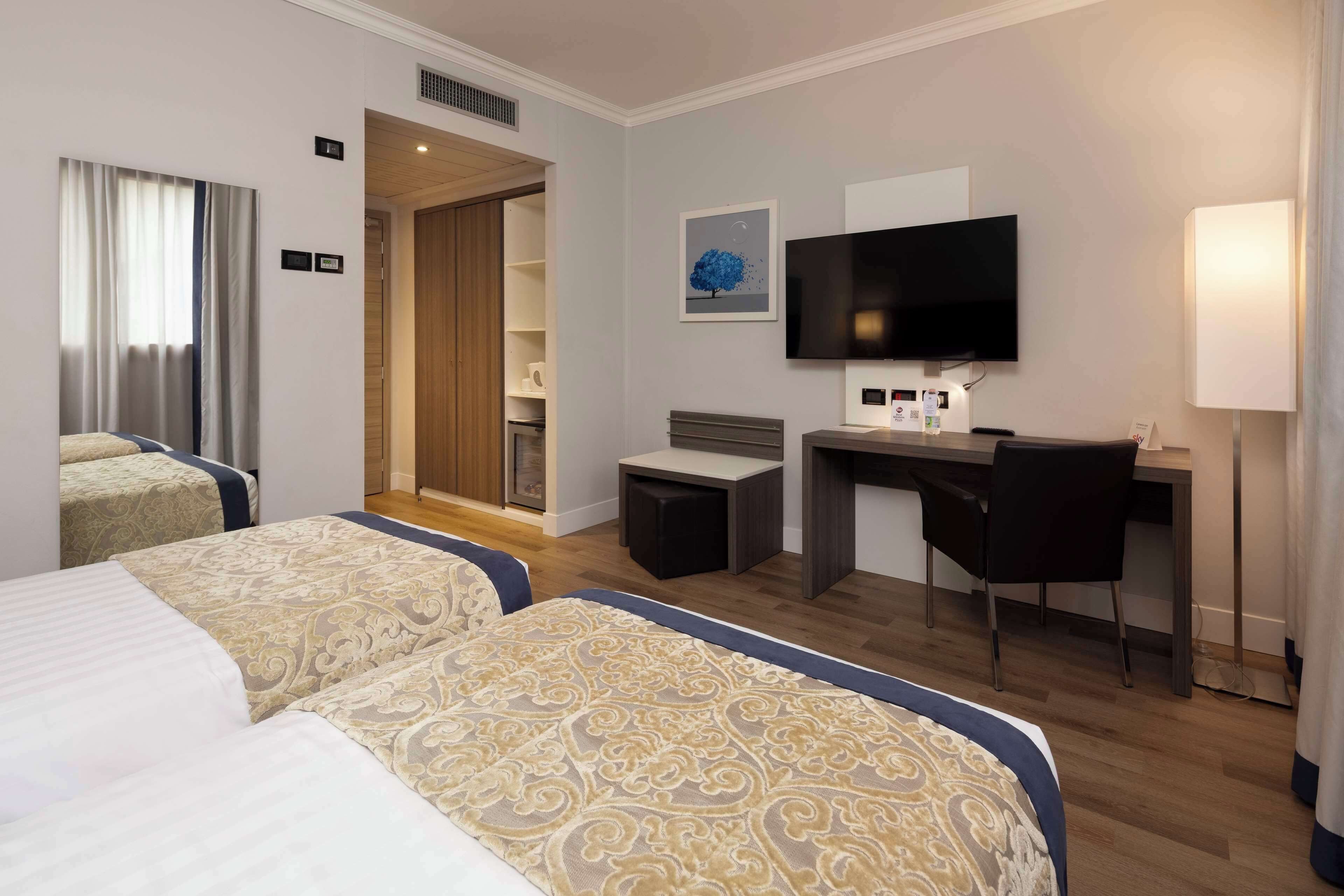 Habitación de hotel con dos camas, un escritorio, un televisor y un pequeño rincón de descanso.