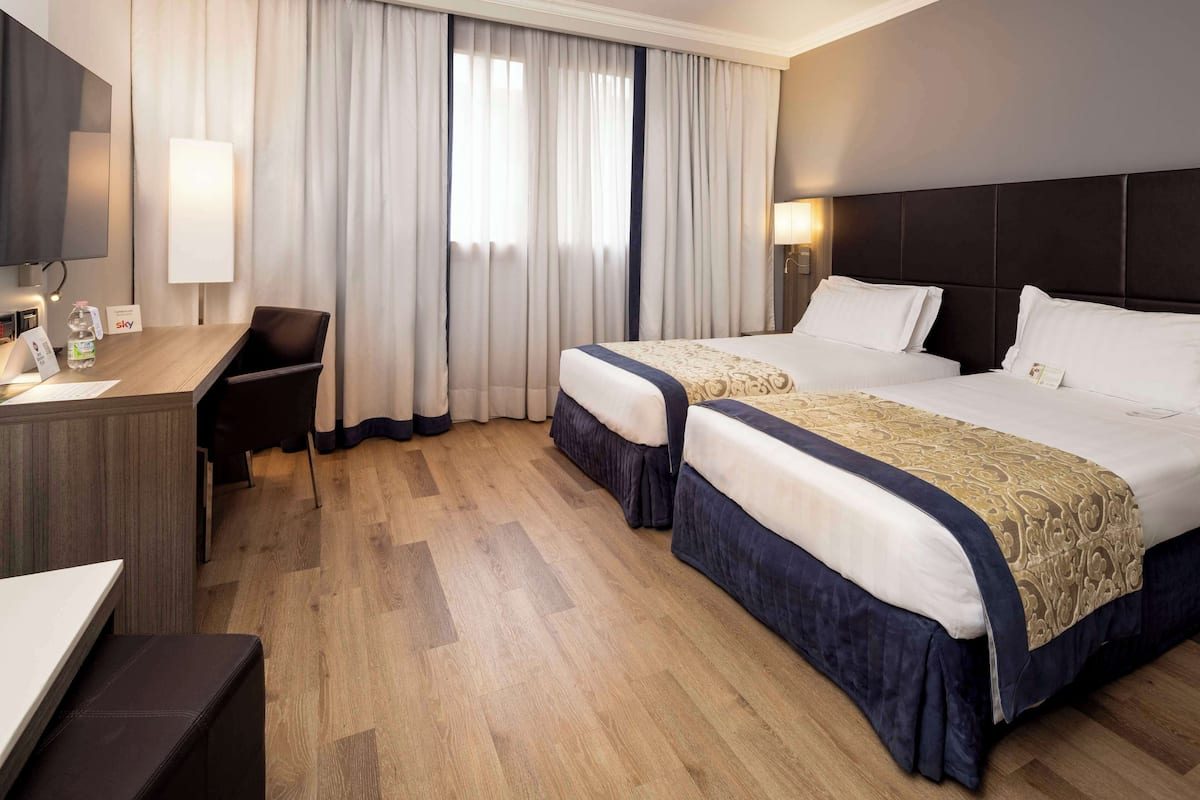 A hotel room with two beds, a desk, a chair, and a television.