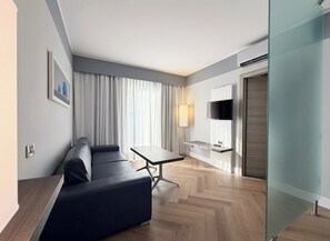 Ein modernes Hotelzimmer mit einer Couch, einem kleinen Tisch, einem Fernseher und einer Glastrennwand.