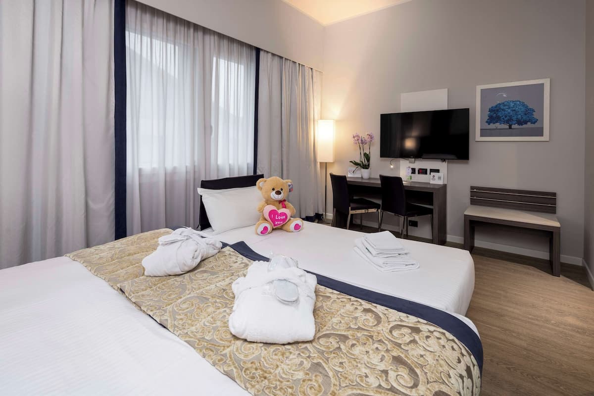 A hotel room with a bed, a desk, a television, and a teddy bear.