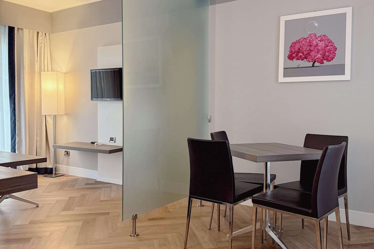 A modern dining area with a glass partition, a table with chairs, a lamp, and a framed picture on the wall.