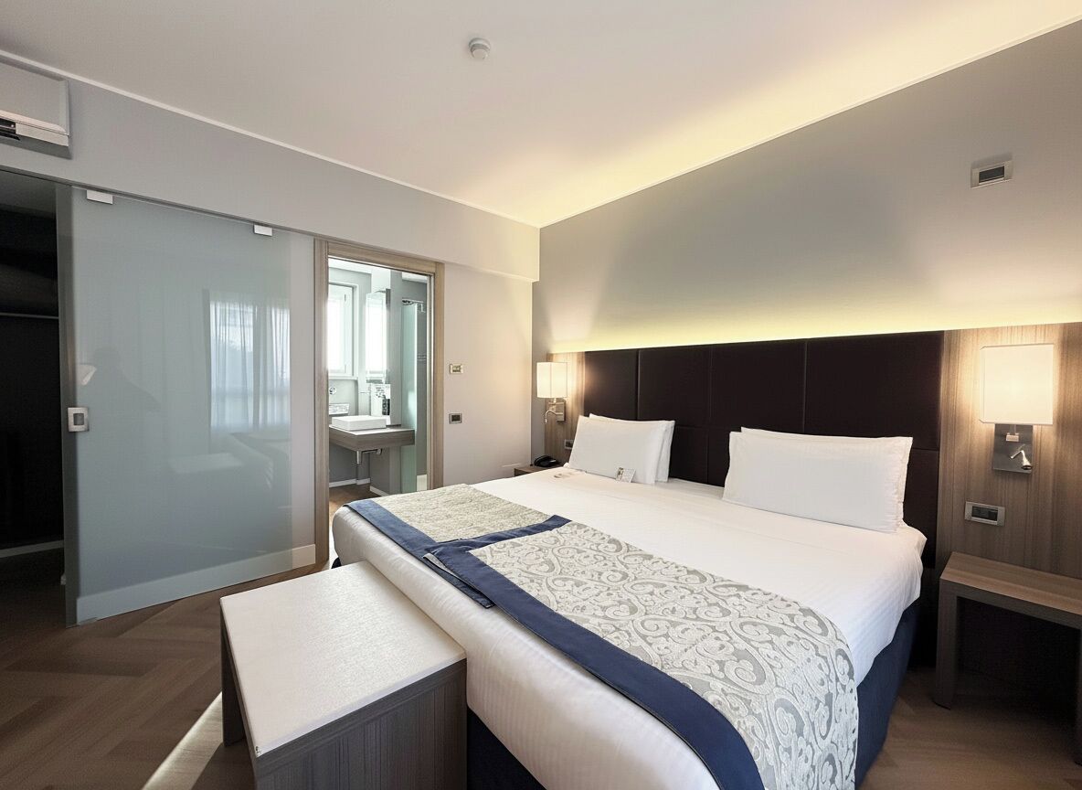 A modern hotel room with a large bed, bedside tables, a desk, and a walk-in closet.