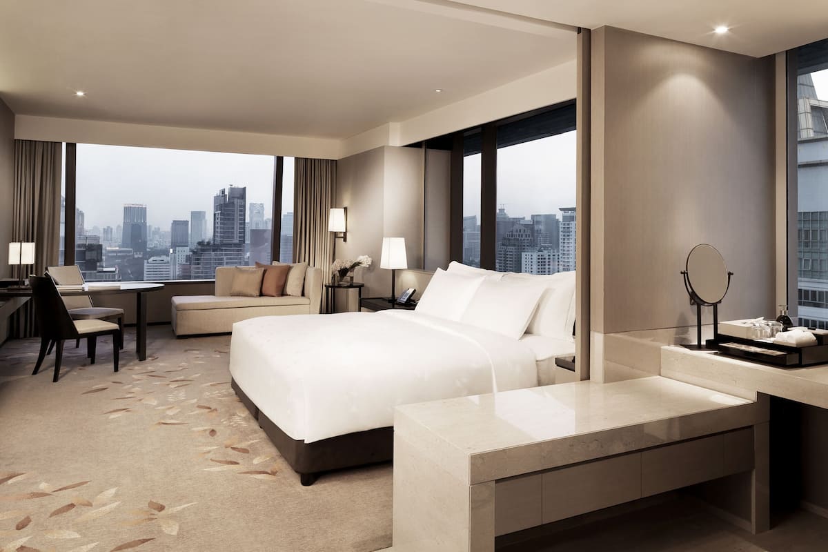 Una habitación de hotel moderna con una cama grande, un escritorio, un sofá y vistas a la silueta urbana.