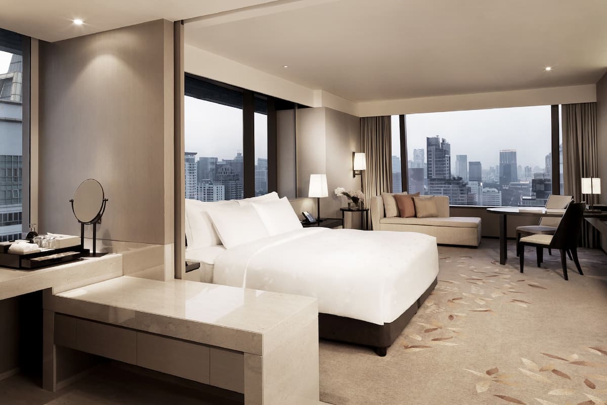 Una habitación de hotel moderna con una cama grande, un escritorio, un sofá y vistas a la ciudad.