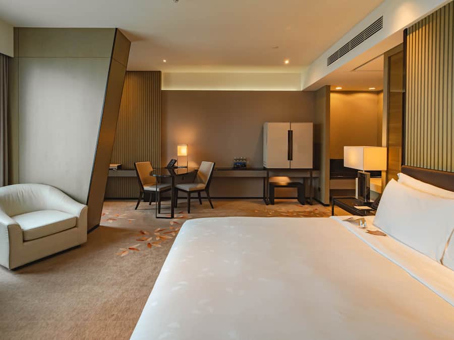A hotel room with a large bed, a desk with a chair, a refrigerator, and a minibar.