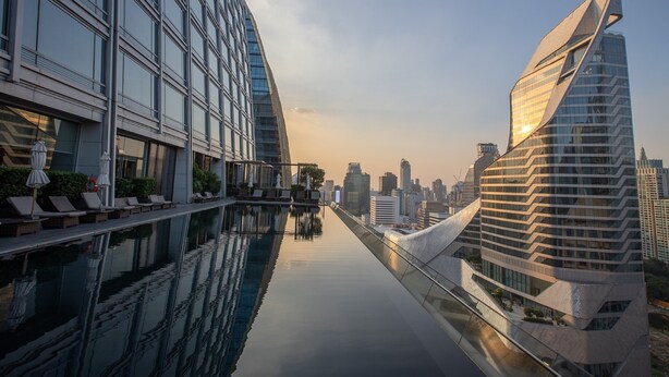 Un hôtel moderne doté d’une piscine aux eaux scintillantes, d’une architecture contemporaine et offrant une vue sur le panorama urbain en arrière-plan.