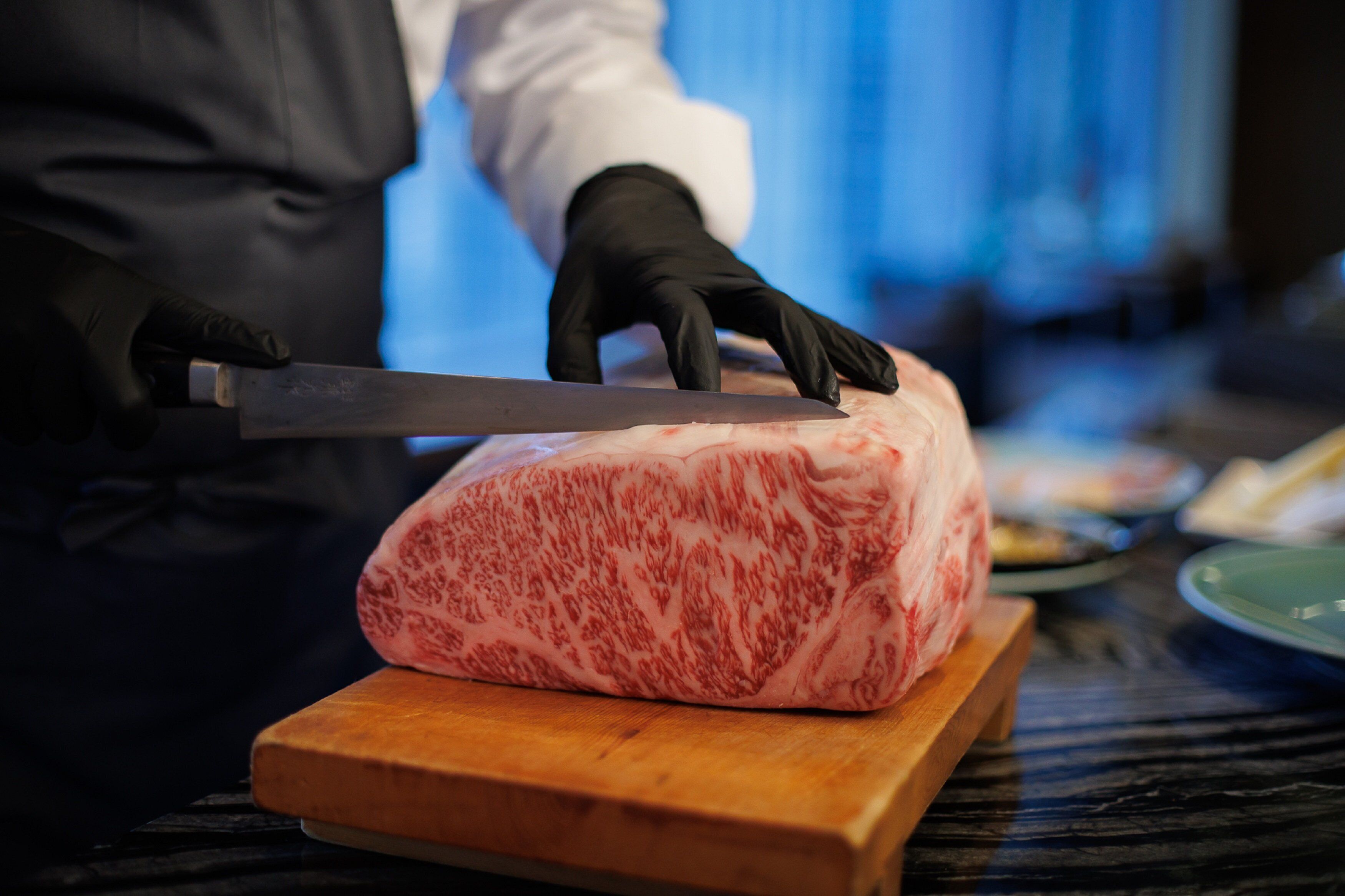 A person cutting a large piece of meat on a wooden cutting board.