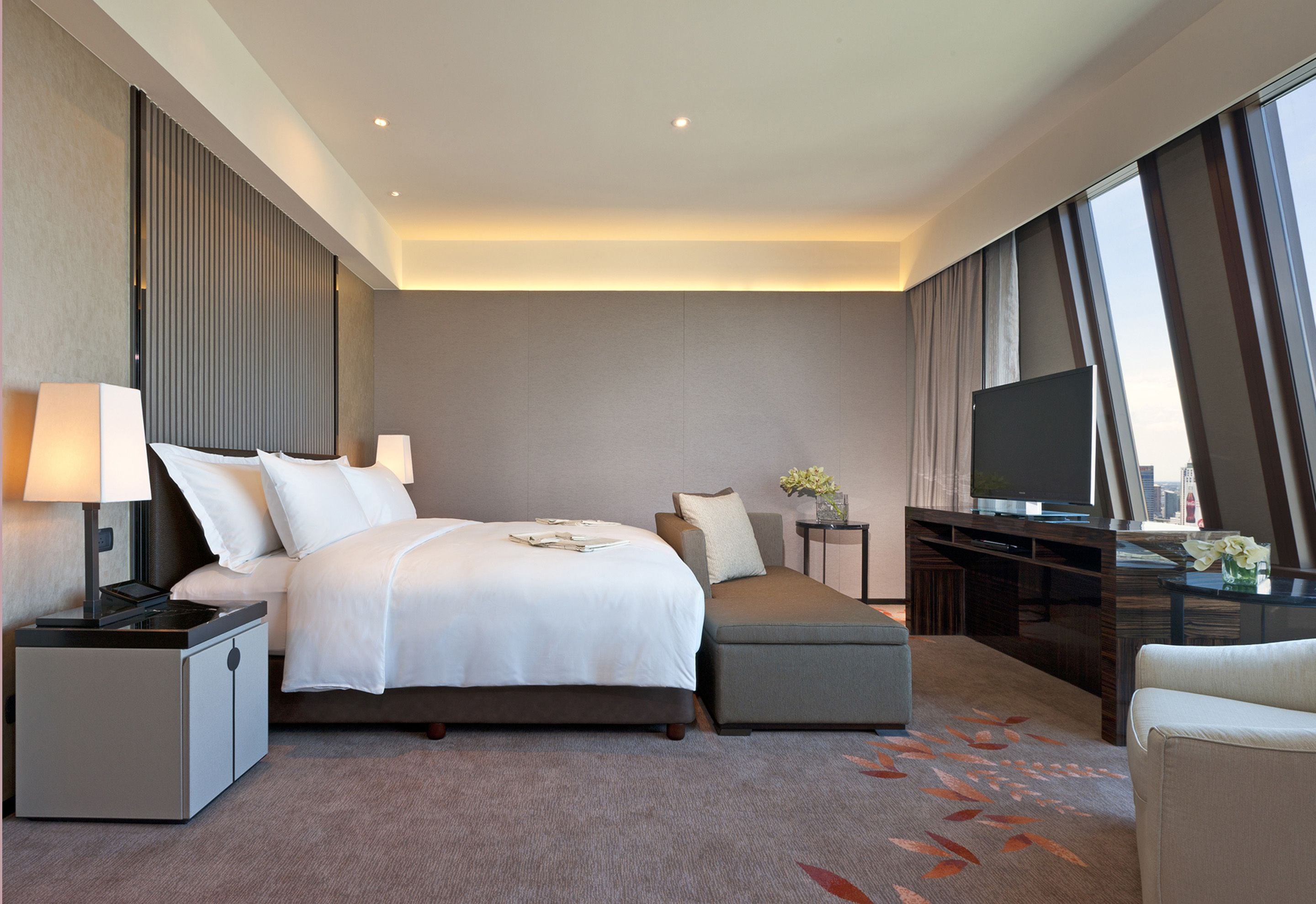 Una habitación de hotel moderna con una cama grande, un sofá, un televisor y vistas a la ciudad.