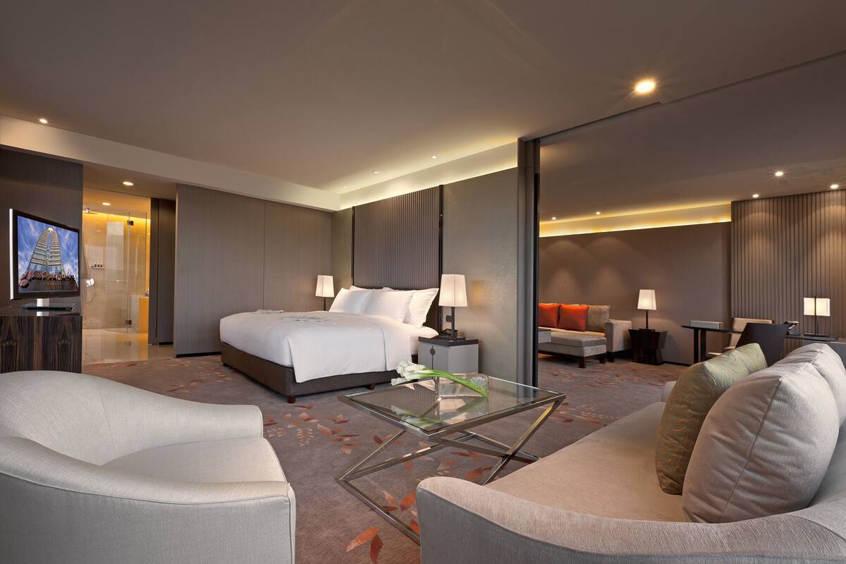 Una habitación de hotel moderna con una cama grande, un sofá, una mesa de centro de vidrio y un televisor.
