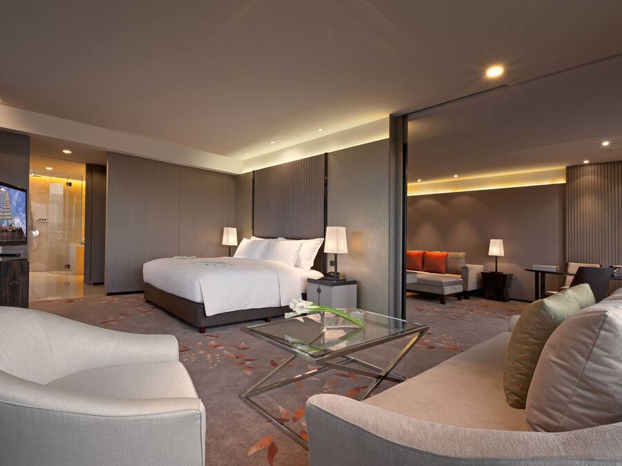 A modern hotel room with a large bed, a sofa, a glass coffee table, and a TV.