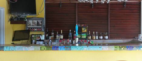 A bar area with a tiled counter, wooden chairs, a television, and various bottles and glasses.