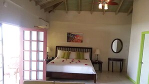 Ein Schlafzimmer mit Bett, Nachttischen, einem Sessel, Deckenventilator, Fenster und Tür.