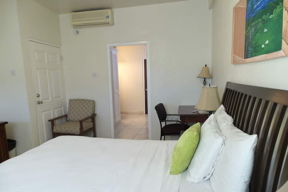 A hotel room with a bed, a chair, a desk, and a lamp.