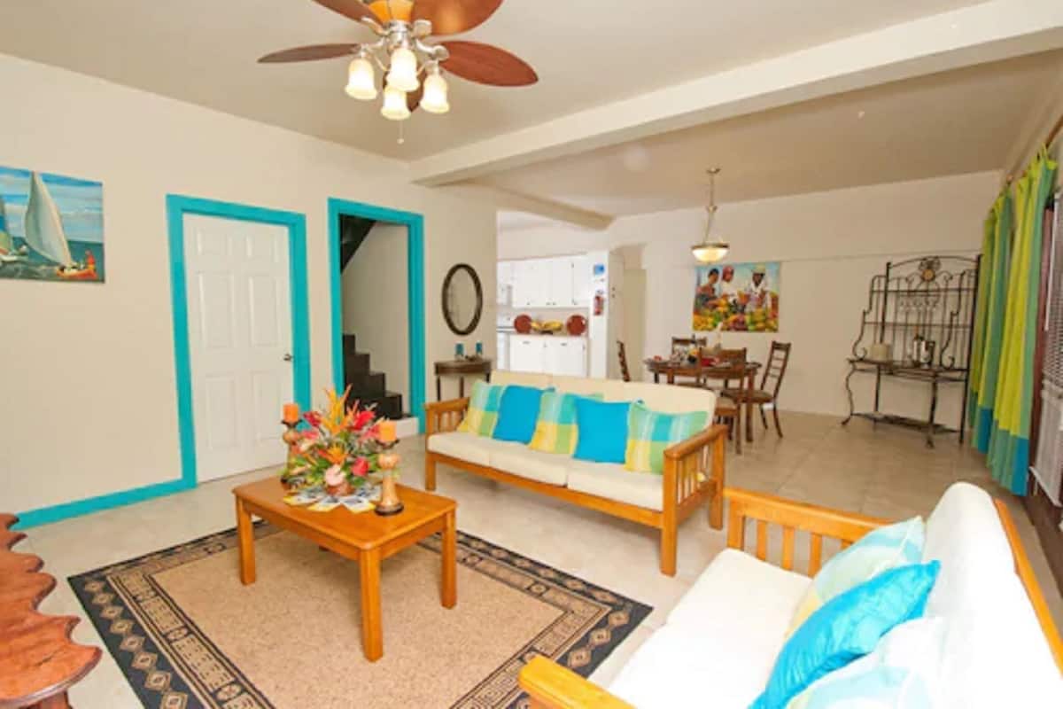 A living room with a sofa, coffee table, and a ceiling fan. There is a dining area with a table and chairs.