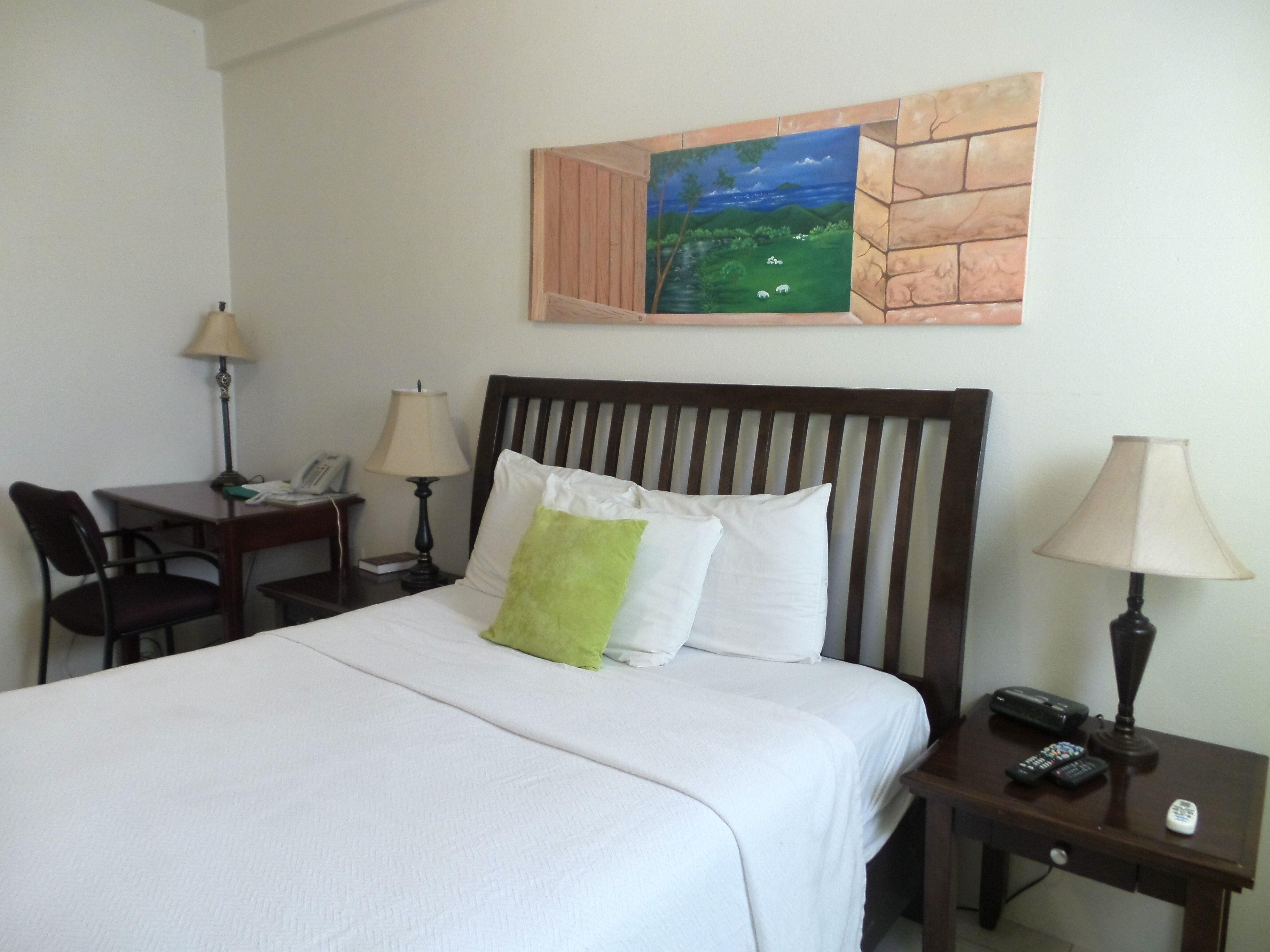 Une chambre d’hôtel avec un lit, deux tables de chevet, un bureau avec une chaise et un tableau au mur.