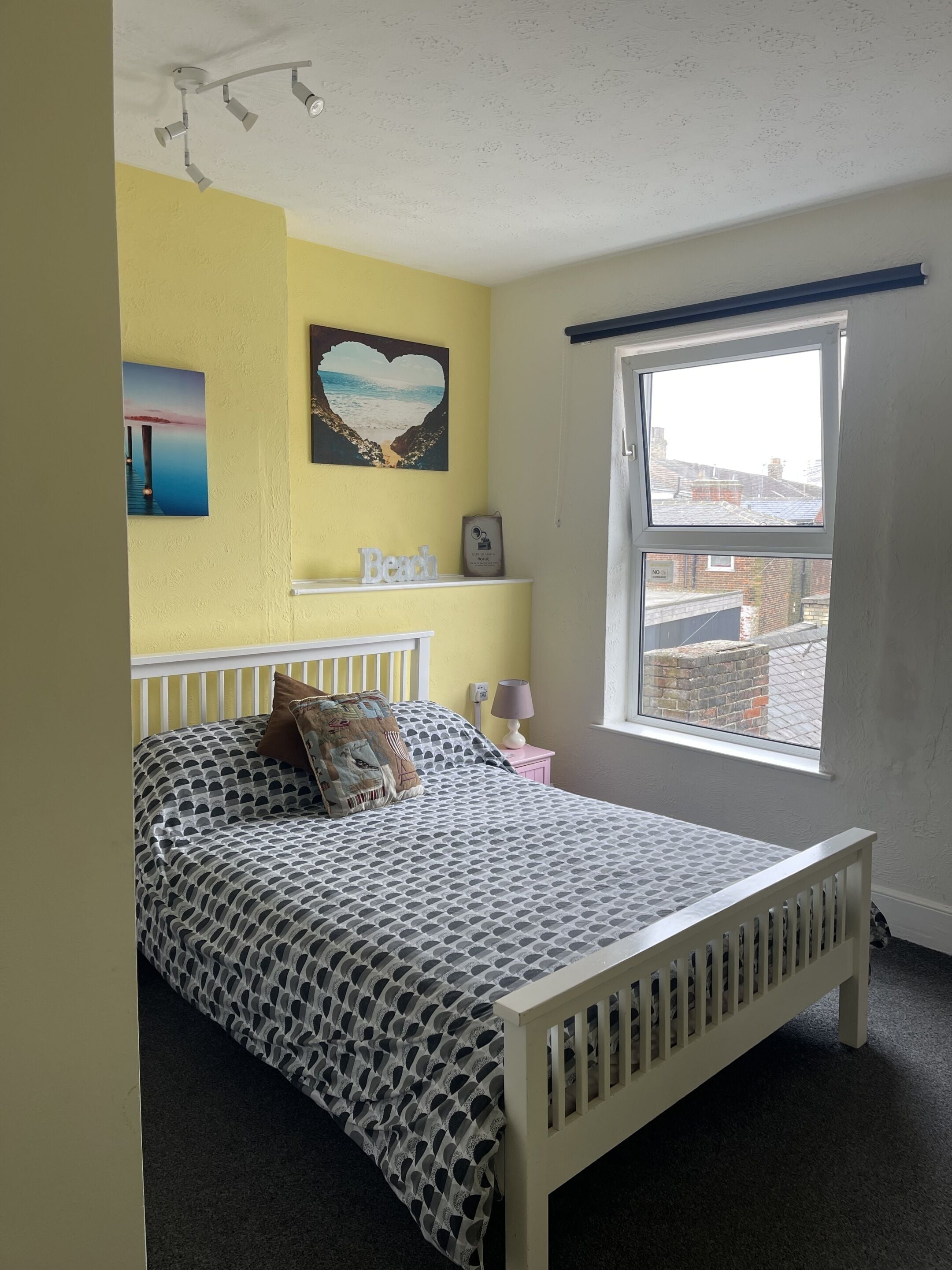 Un dormitorio con cama, ventana, estante en la pared y lámpara en el techo.