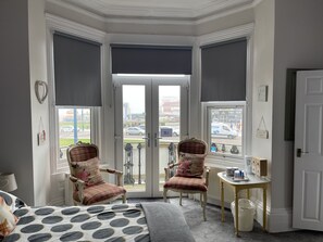 A room with a bed, two chairs, a small table, and a view through a door. - Henry's On The Prom (Great Yarmouth)