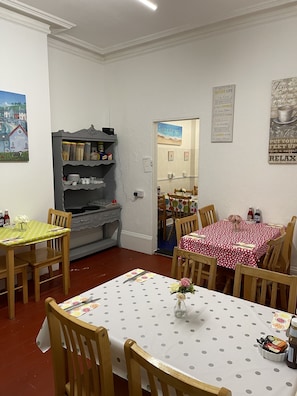 A dining area with a table set for four, a shelf with kitchen items, and a painting on the wall. - Henry's On The Prom (Great Yarmouth)