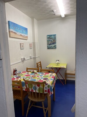 Ein kleiner Essbereich mit einem Tisch, der mit einer Tischdecke mit Punkten bedeckt ist, Holzstühle und ein kleiner Tisch mit einer gelben Tischdecke.