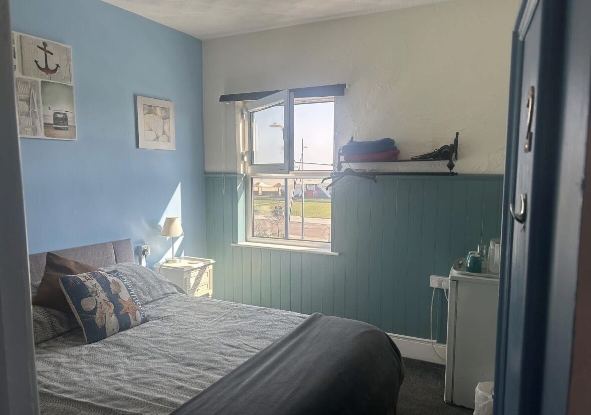 A bedroom with a bed, a window, a nightstand, and a dresser.