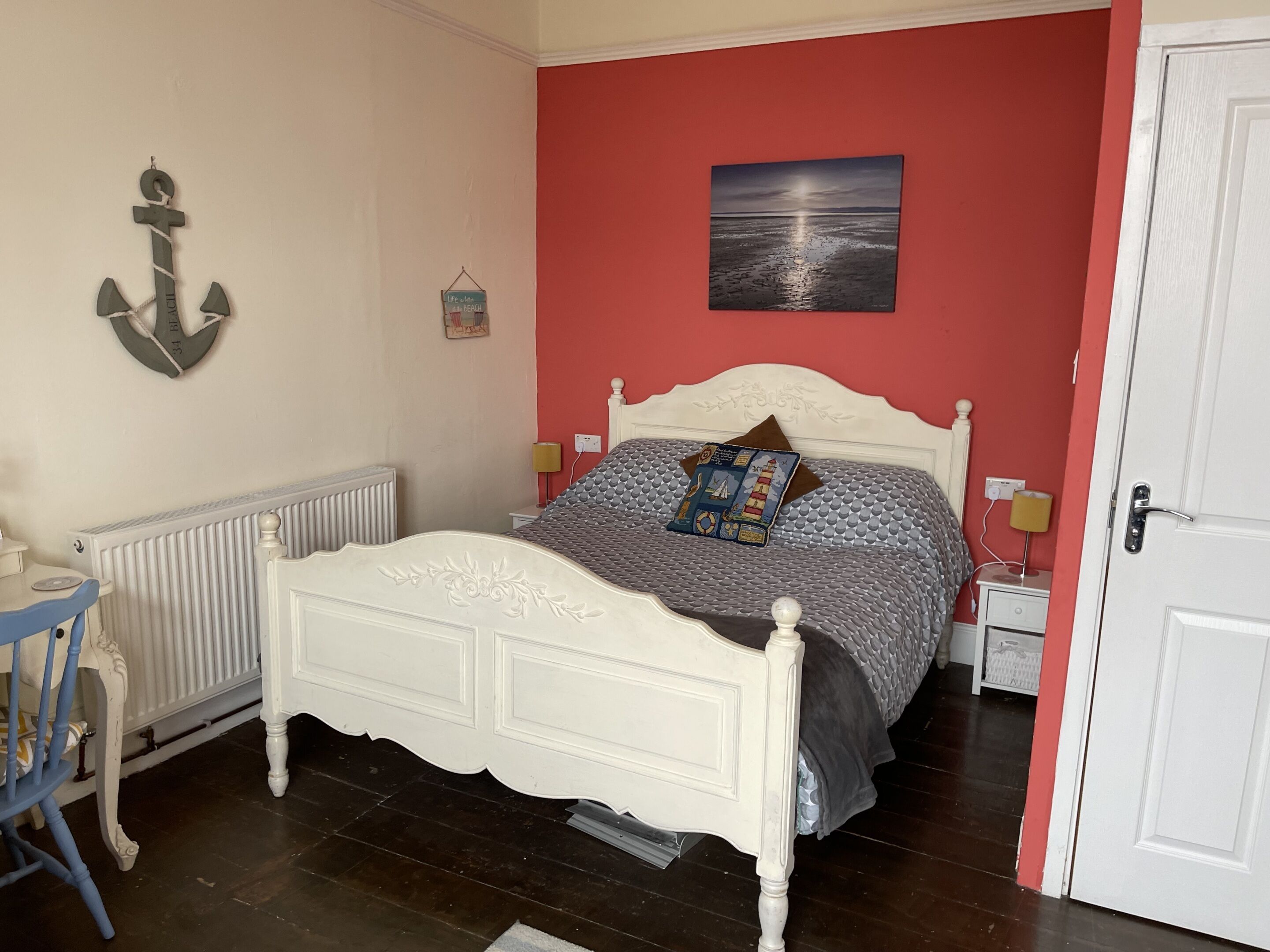 A bedroom with a white bed, red walls, a nightstand, a lamp, a radiator, and a door.