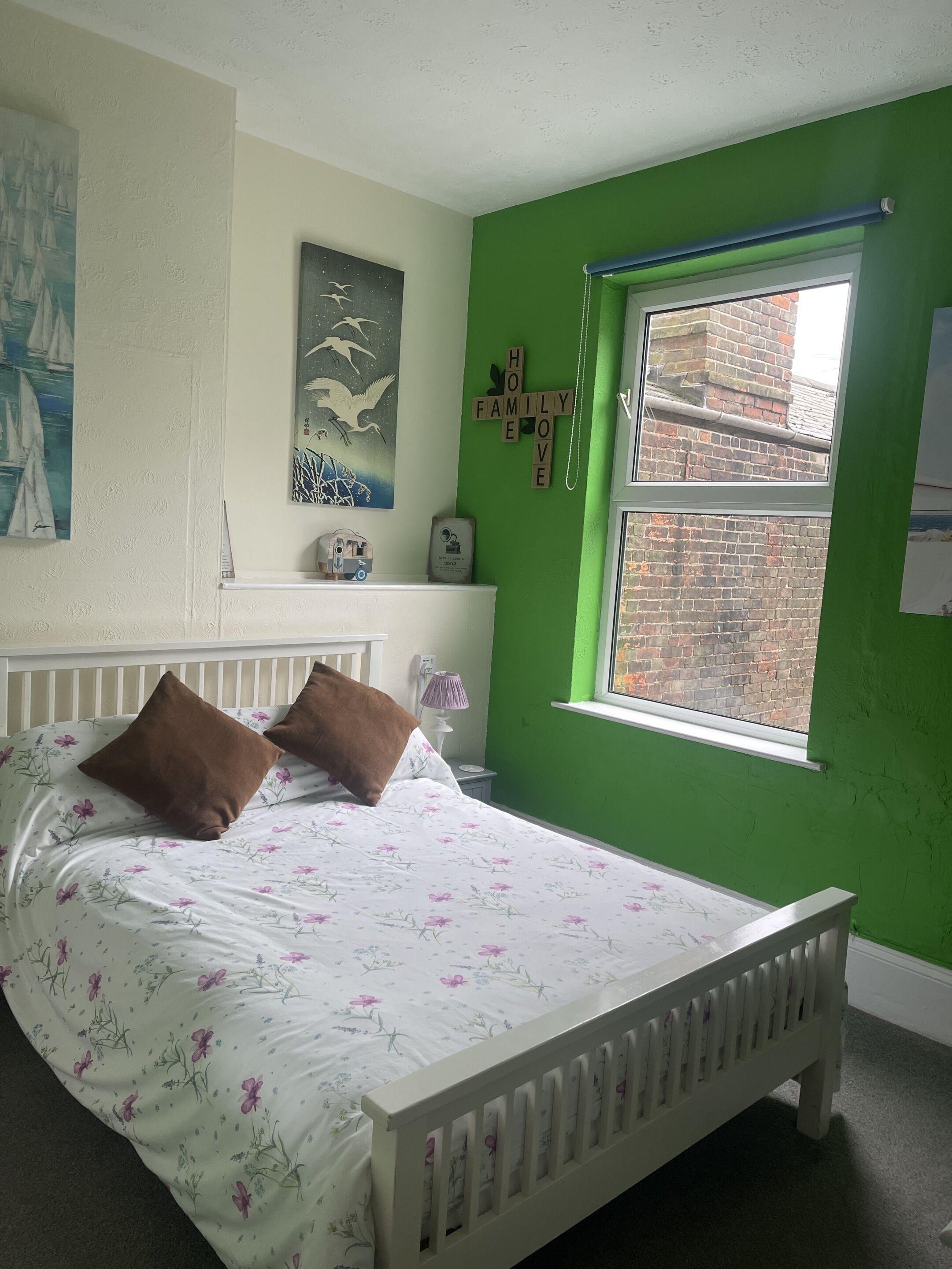 A bedroom with a bed, pillows, a nightstand, a lamp, a window, and a wall with a green paint color.