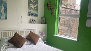 A bedroom with a bed, pillows, a nightstand, a lamp, a window, and a wall with a green paint color.