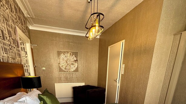 A hotel room with a bed, green pillows, a green quilted bedspread, a wall clock, a framed picture, and a door. - Delovely Hotel (Blackpool)