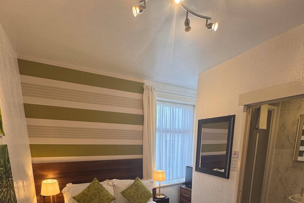 A hotel room with a bed, bedside lamps, a shower, and a window with curtains.