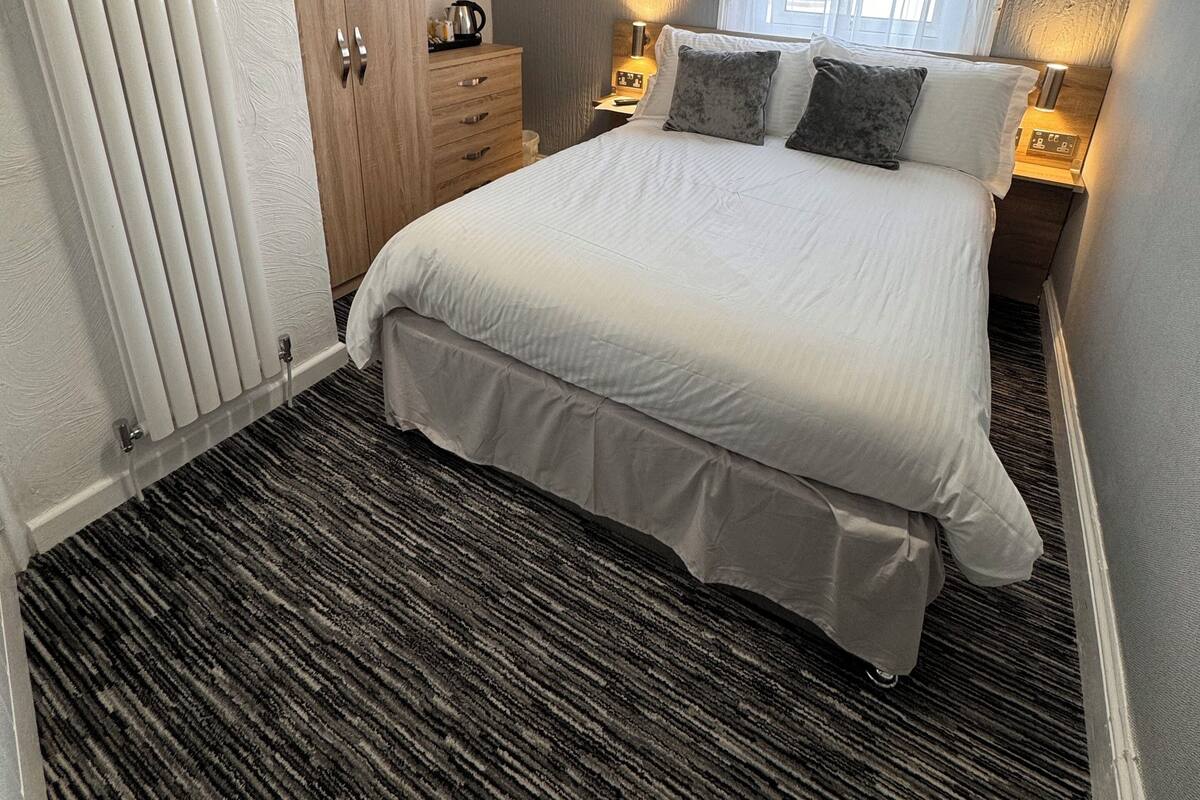 A bedroom with a large bed, a wooden wardrobe, a radiator, and a window with curtains.