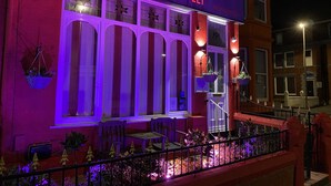 A building with a purple facade and the name 'DE-LOVELY' illuminated in red. There are hanging baskets with plants on the windowsills. - Delovely Hotel (Blackpool)
