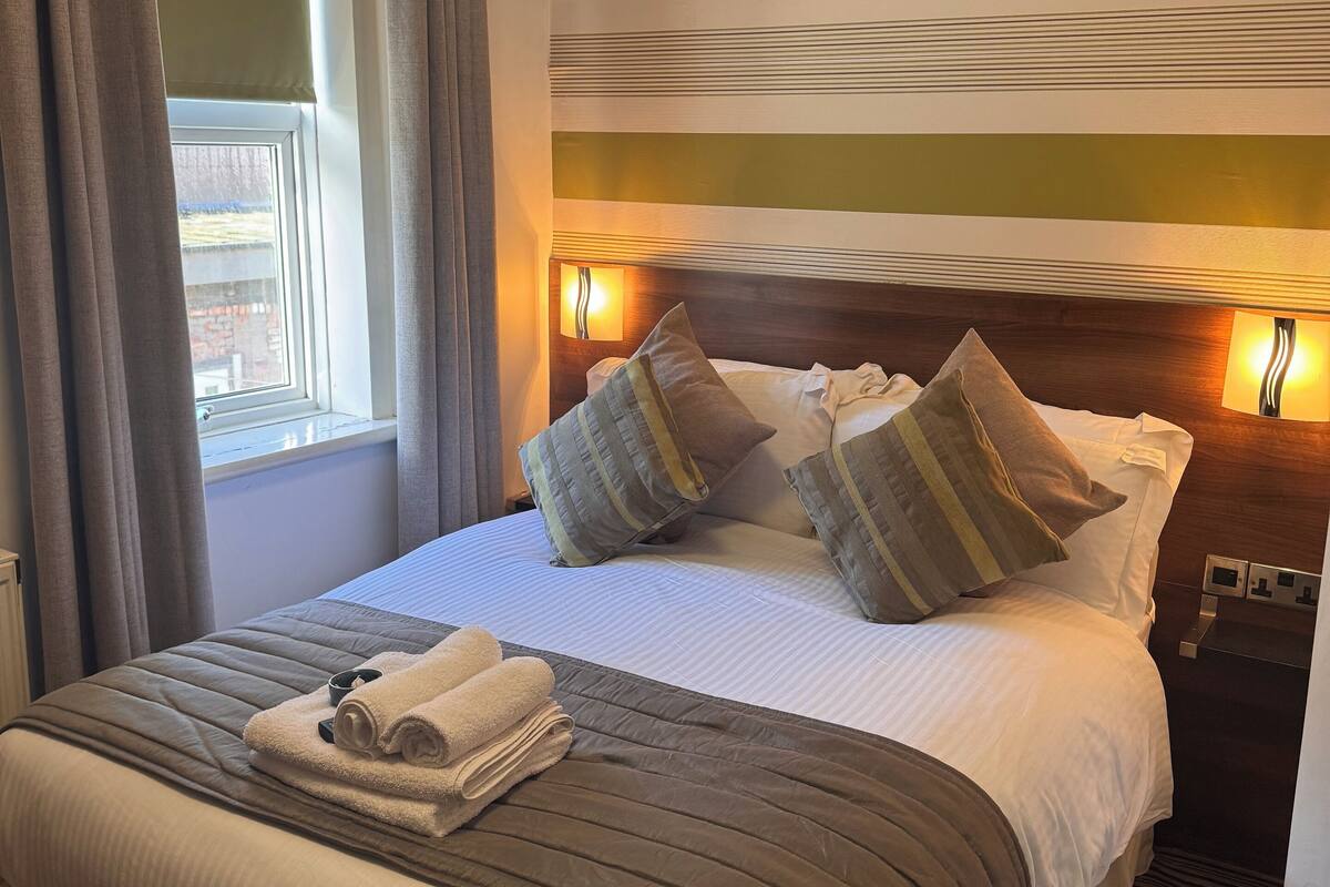 A hotel room with a large bed, two bedside lamps, a window with curtains, and a view of the outside.