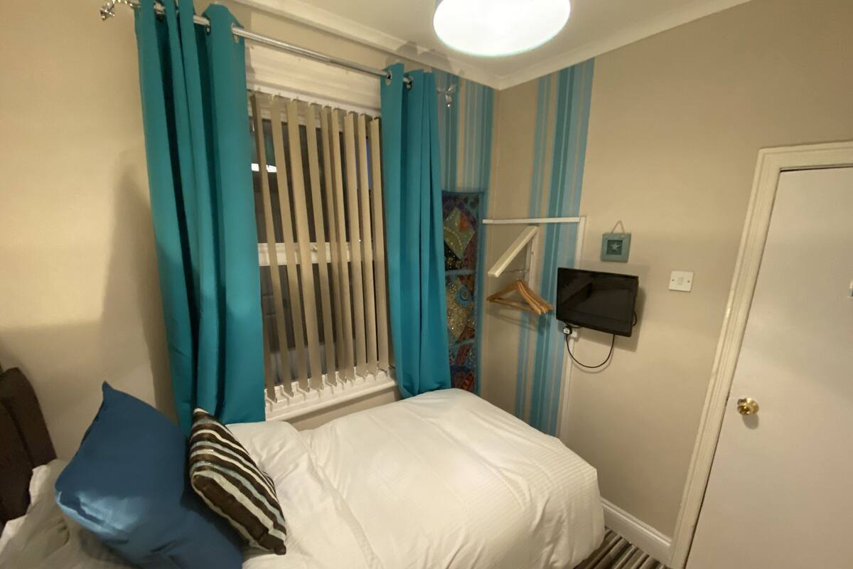 A hotel room with a bed, a hanging coat rack, a television, and a door.