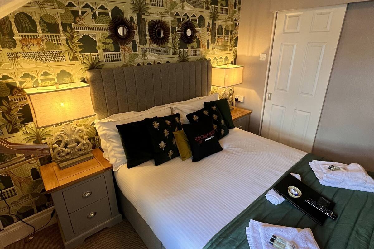 A hotel room with a bed, nightstand, and a wall with a patterned mural.