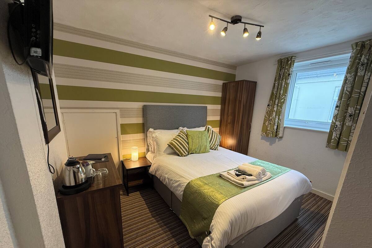 A hotel room with a bed, bedside table, lamp, and a window with curtains.