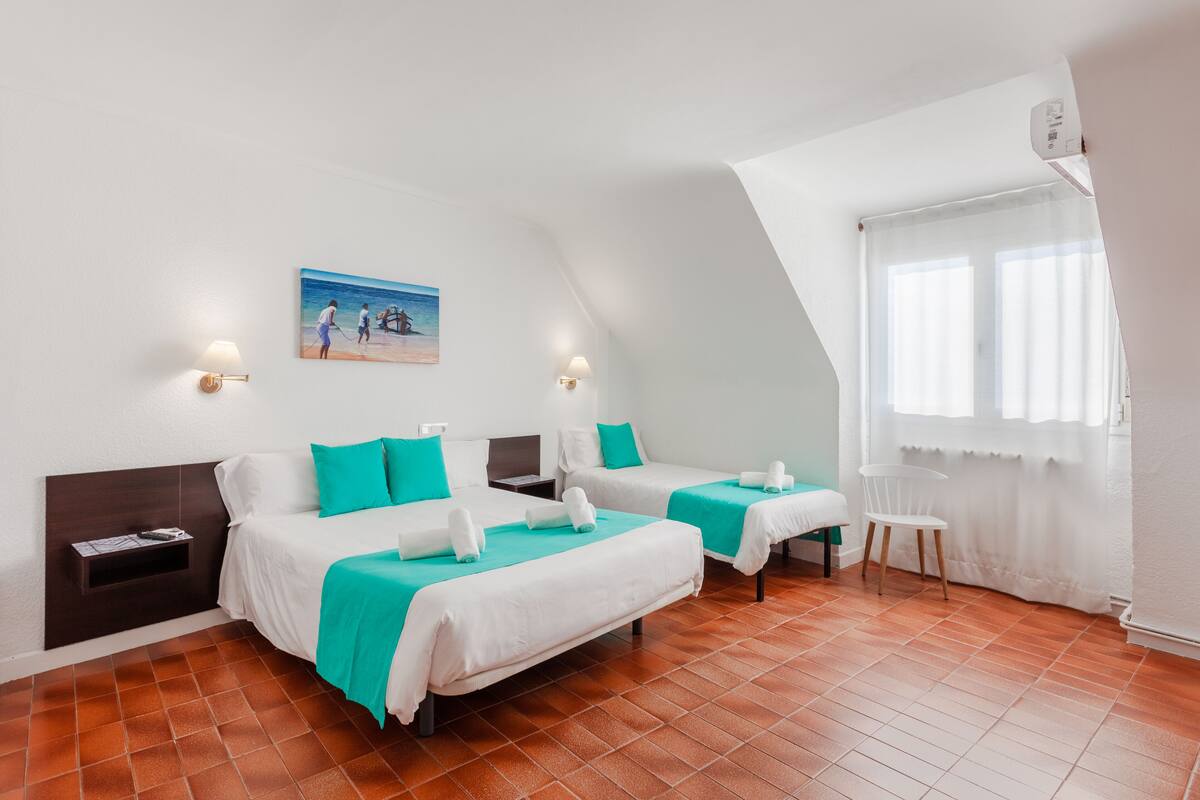 A hotel room with two beds, a painting on the wall, a window with curtains, and a chair.