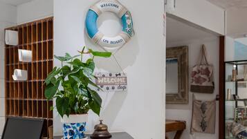 Una habitación con una planta en maceta, un cartel de bienvenida y una estantería con diversos objetos.