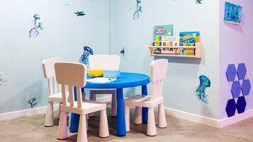 Children can play and learn in this vibrant playroom with a round table, educational posters, and a bookshelf.