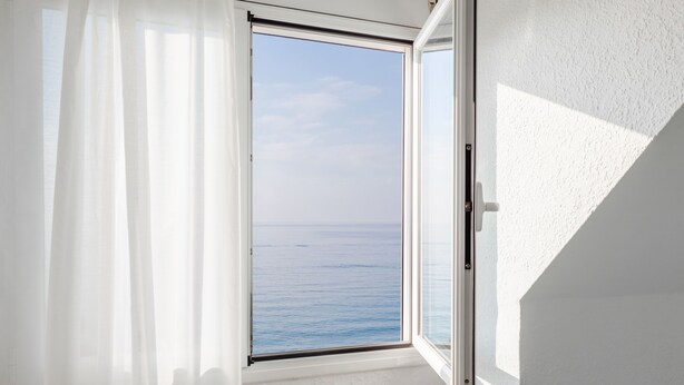 Una habitación con un ventanal grande con vistas a un cuerpo de agua, un radiador blanco y cortinas de encaje.