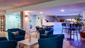 Un amplio salón con sillones tapizados en azul, una mesa de centro blanca y una zona de bar al fondo.