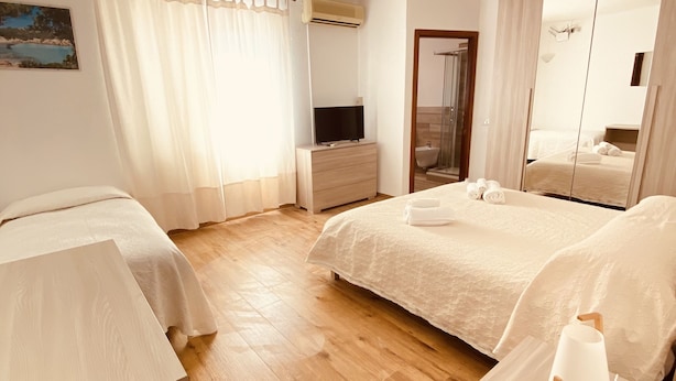 A hotel room with two beds, a wooden floor, a TV, a mirror, and a bathroom visible through an open door. - Affittacamere Ciro's House (Olbia)