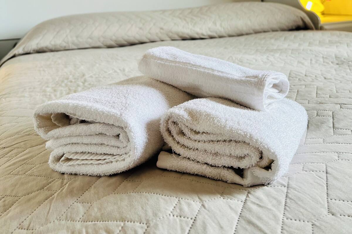 A neatly made bed with a quilted cover, a stack of folded towels, and three wall art pieces depicting abstract designs and flowers.