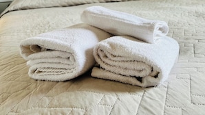 A neatly made bed with a quilted cover, a stack of folded towels, and three wall art pieces depicting abstract designs and flowers. - Affittacamere Ciro's House (Olbia)
