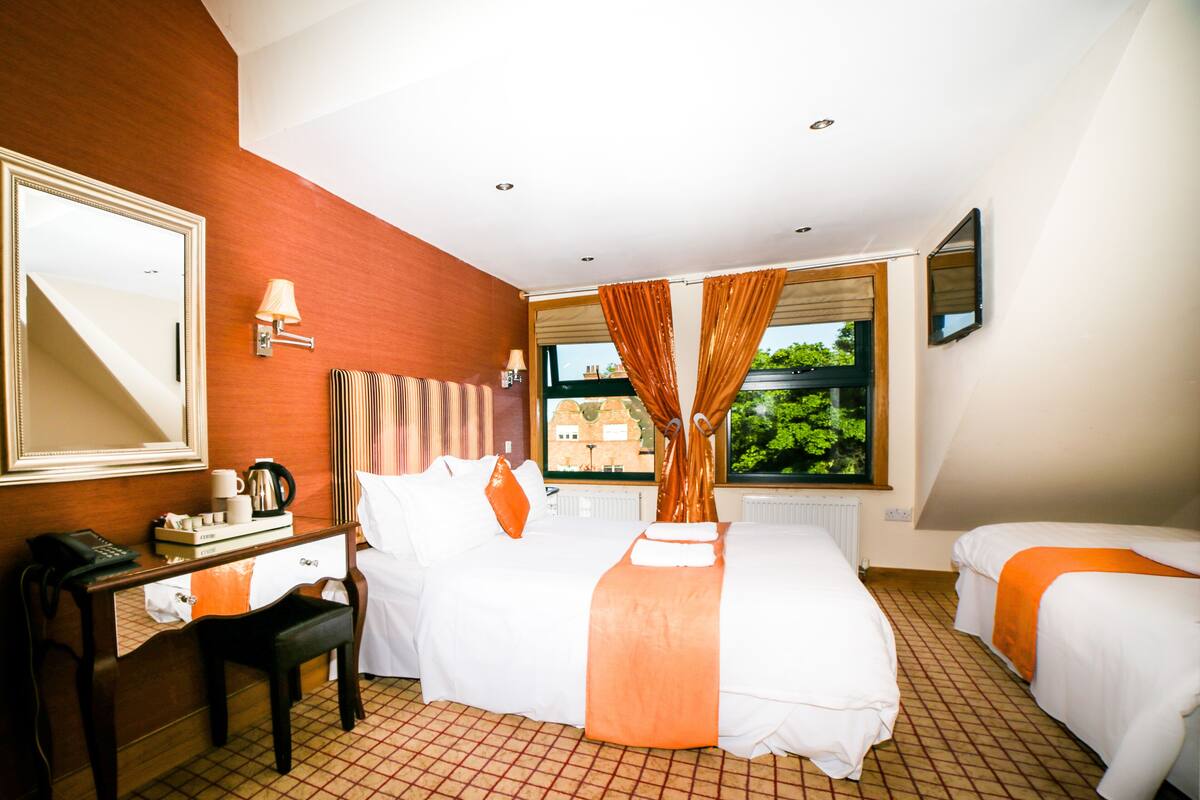 A hotel room with a bed, a desk, a chair, a telephone, and a window with curtains.