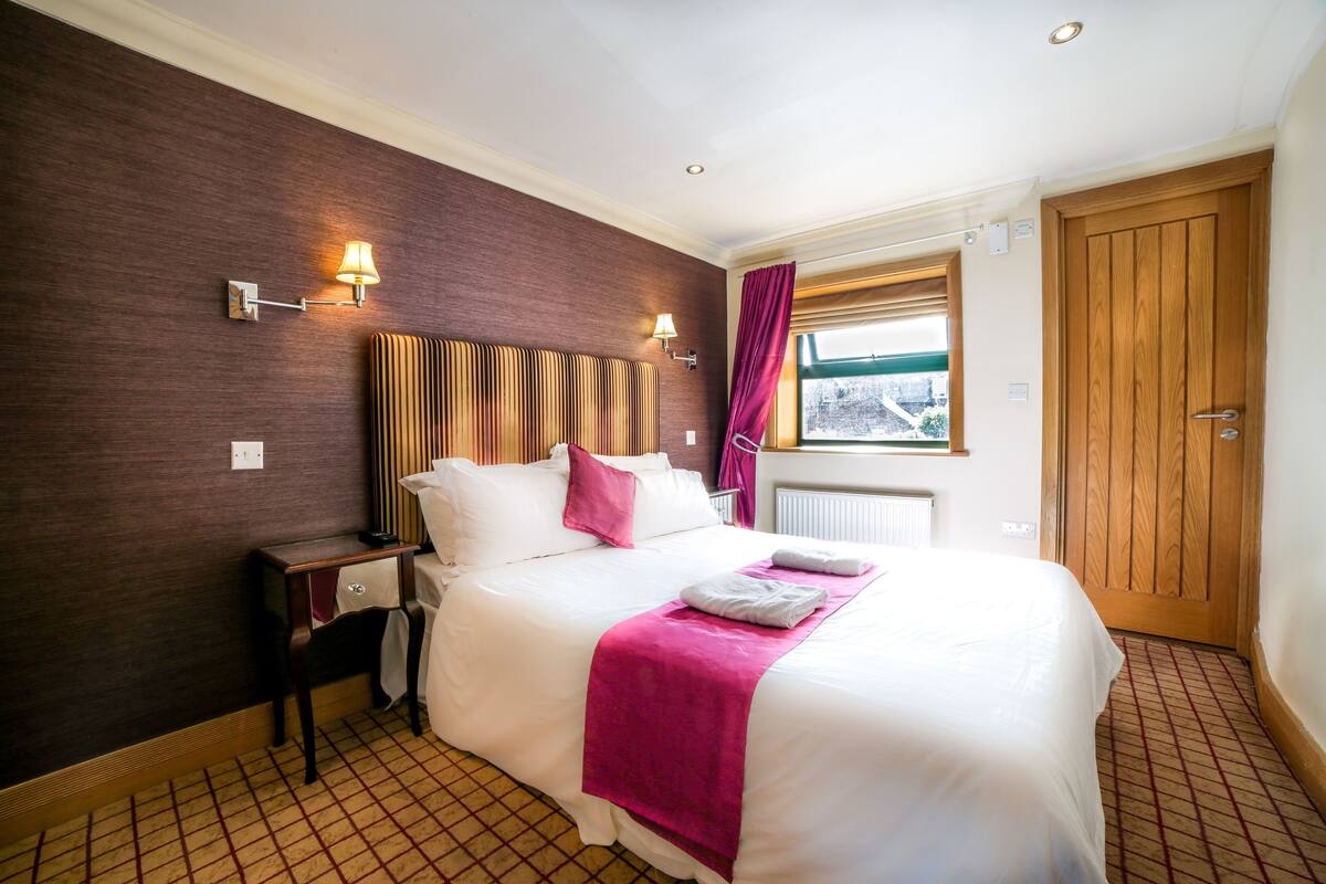 A hotel room with a bed, nightstand, lamp, and window with curtains.